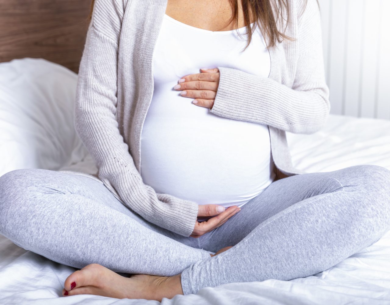 Closeup of a pregnant woman sitting on the bed at home holding her baby belly